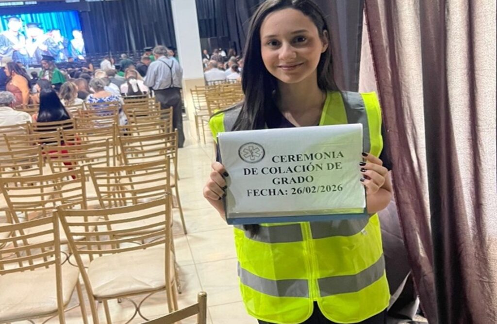 Voluntaria de UNISUD con chaleco de seguridad sostiene un letrero en el salón durante la colación de grado.