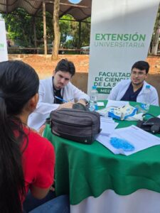 Dos estudiantes de medicina de UNISUD brindan atención médica comunitaria a una paciente al aire libre.